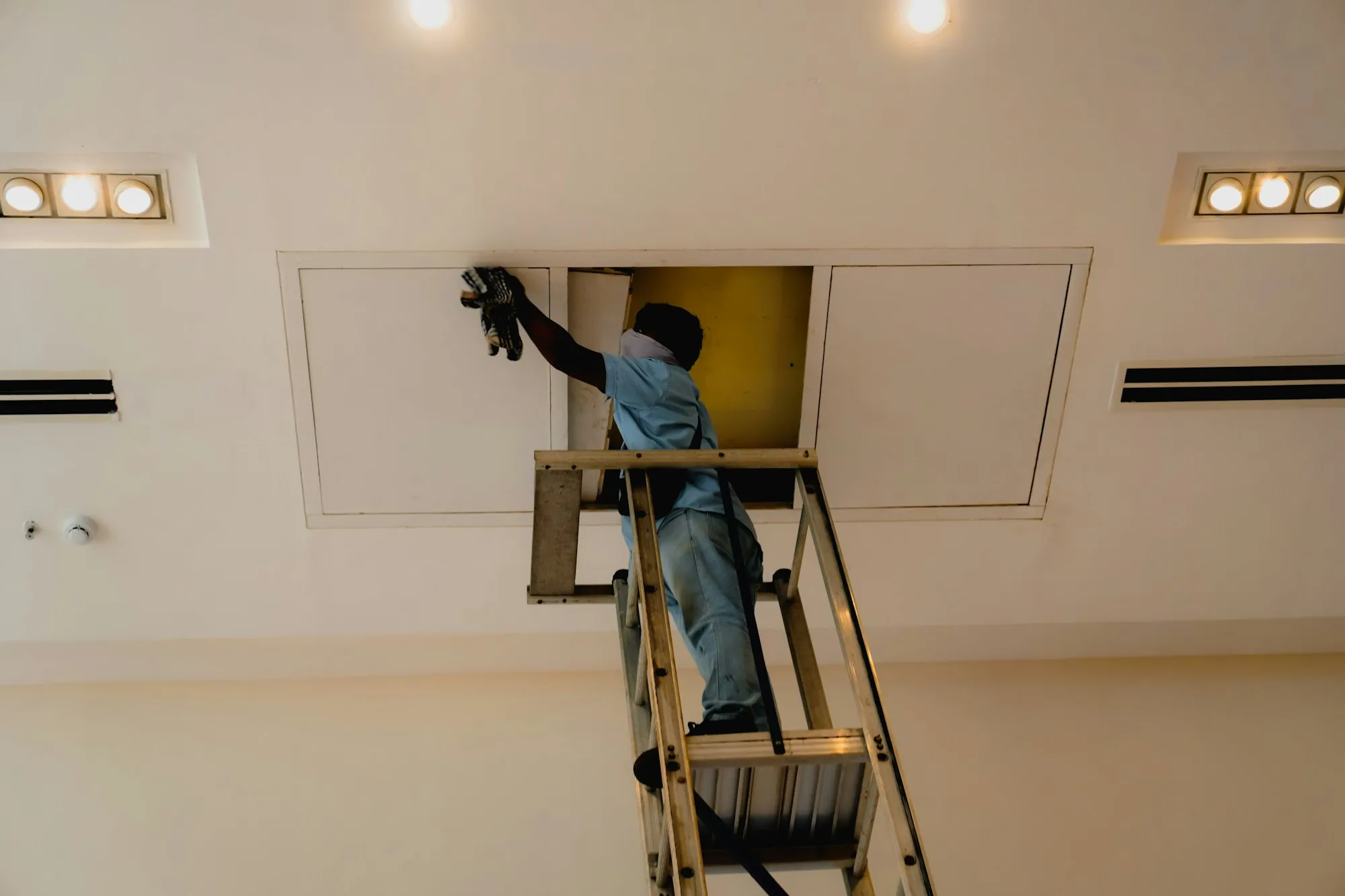 Cleaner on a ladder dusting a ceiling vent