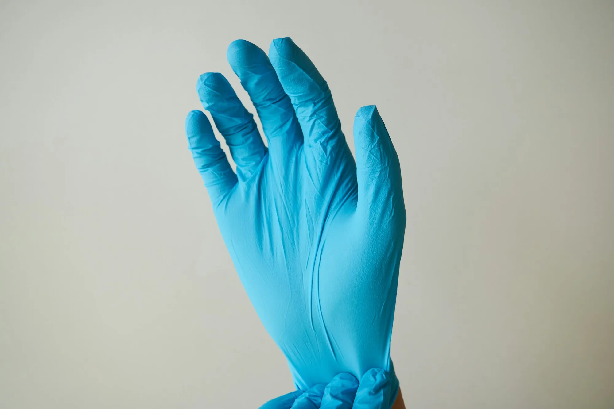 Hand in a blue glove against a white wall