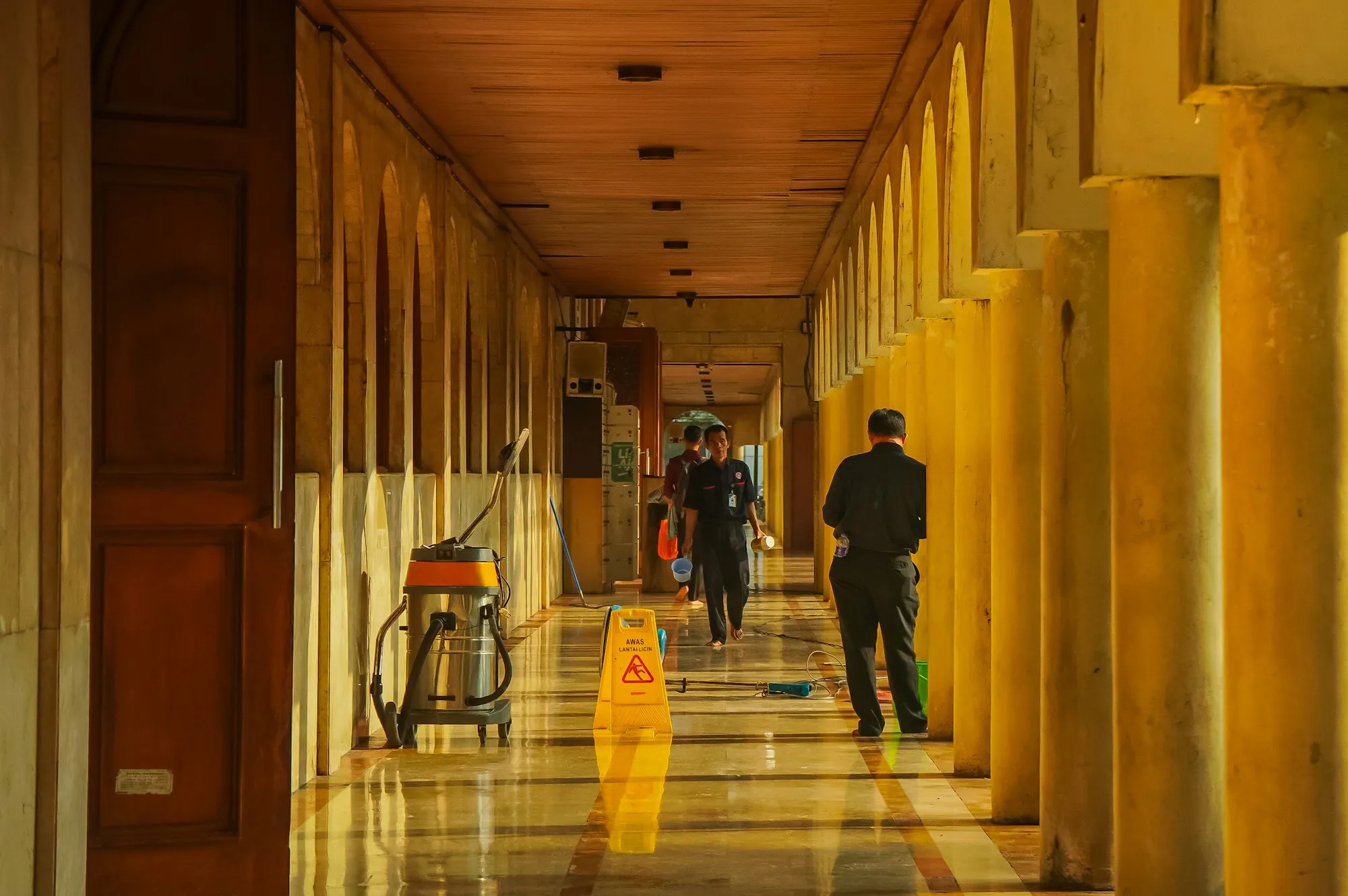 Cleaner working down a long arched corridor with a wet floor sign